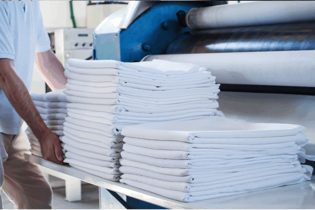 Lenzuola bianche piegate e pulite all'interno di una lavanderia industriale.