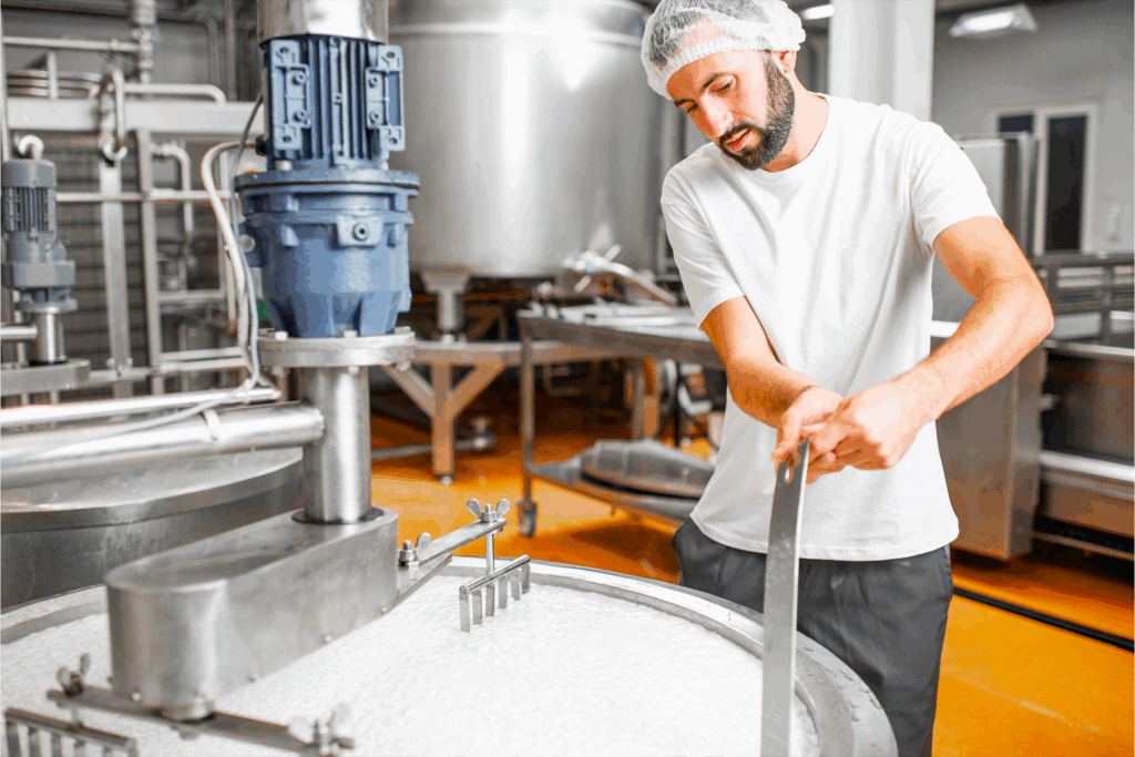 Casaro all'interno del laboratorio sta girando il mestolo nel calderone contenente caglio e latte