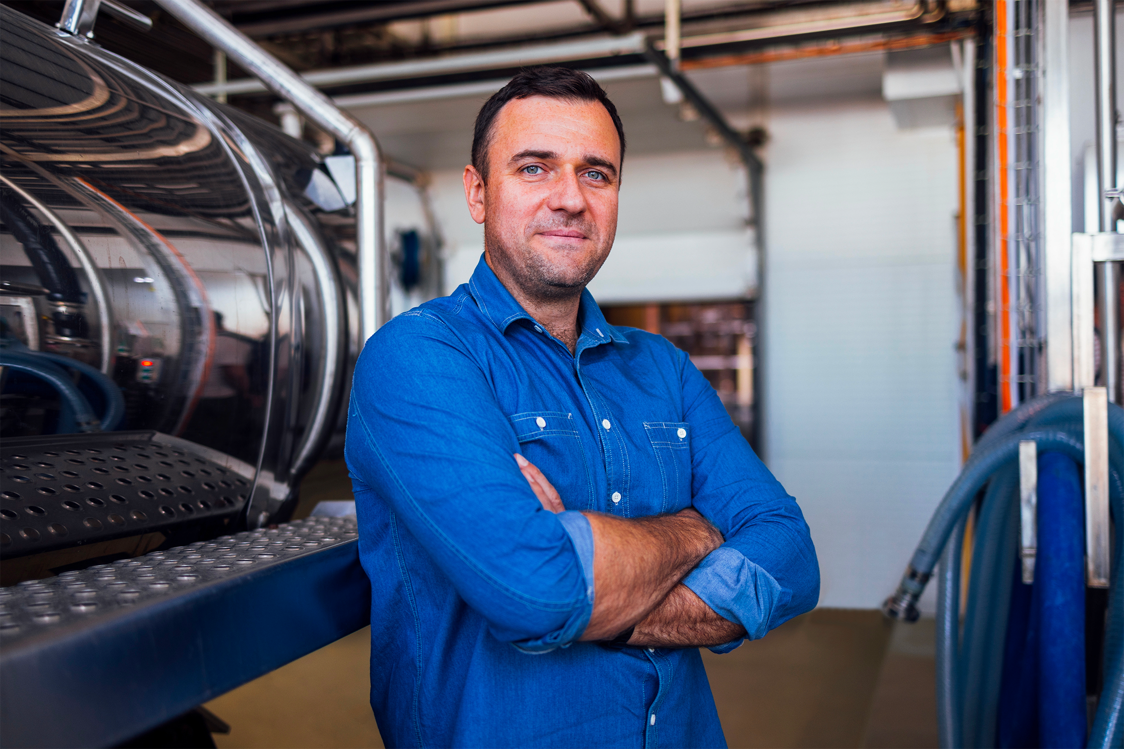 Responsabile di produzione sorride con le braccia conserte a fianco ad silos dentro un magazzino di produzione.