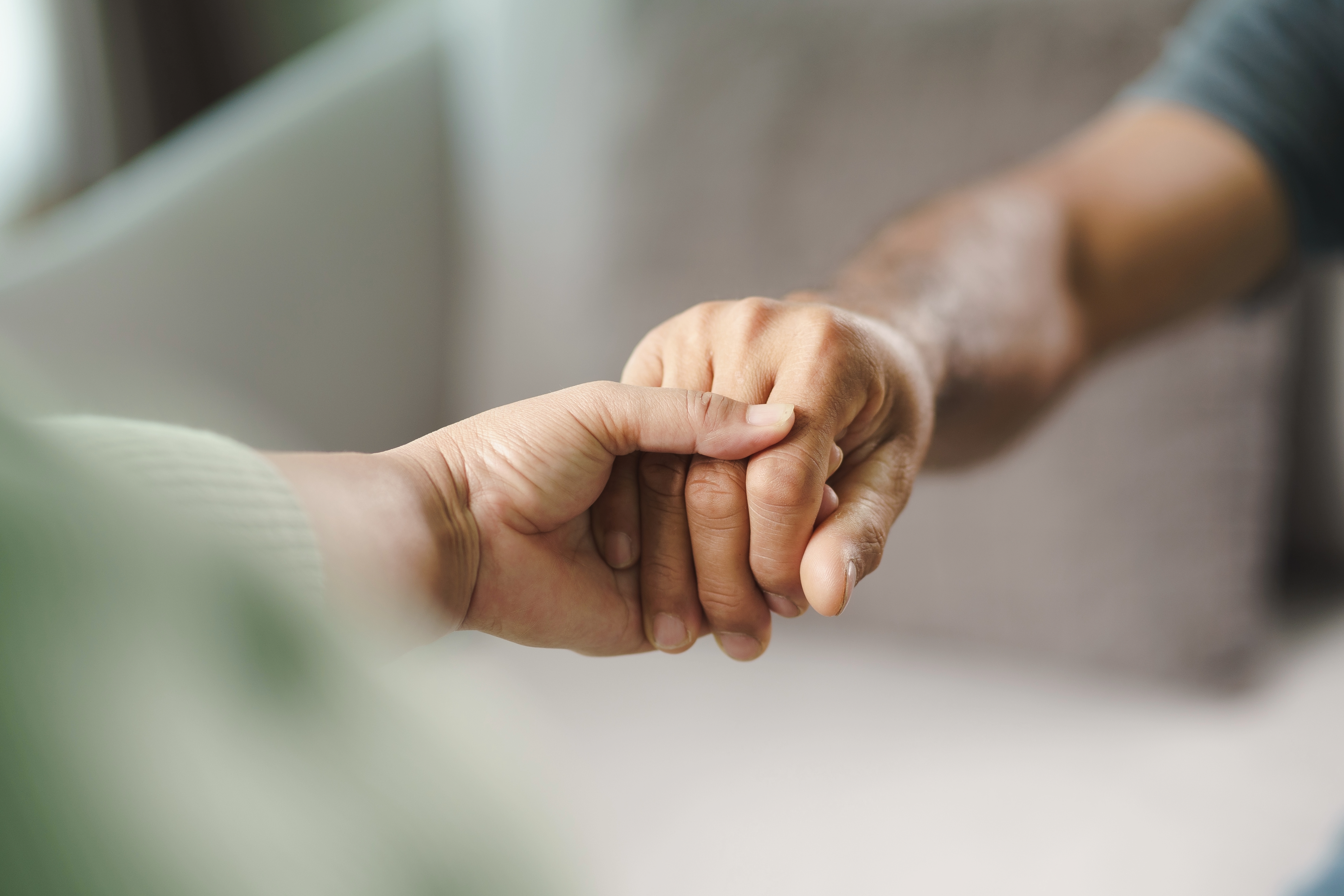 Inquadratura stretta su due mani che si stringono. La mano di una donna che stringe la mano di un uomo come a donargli conforto e aiuto.