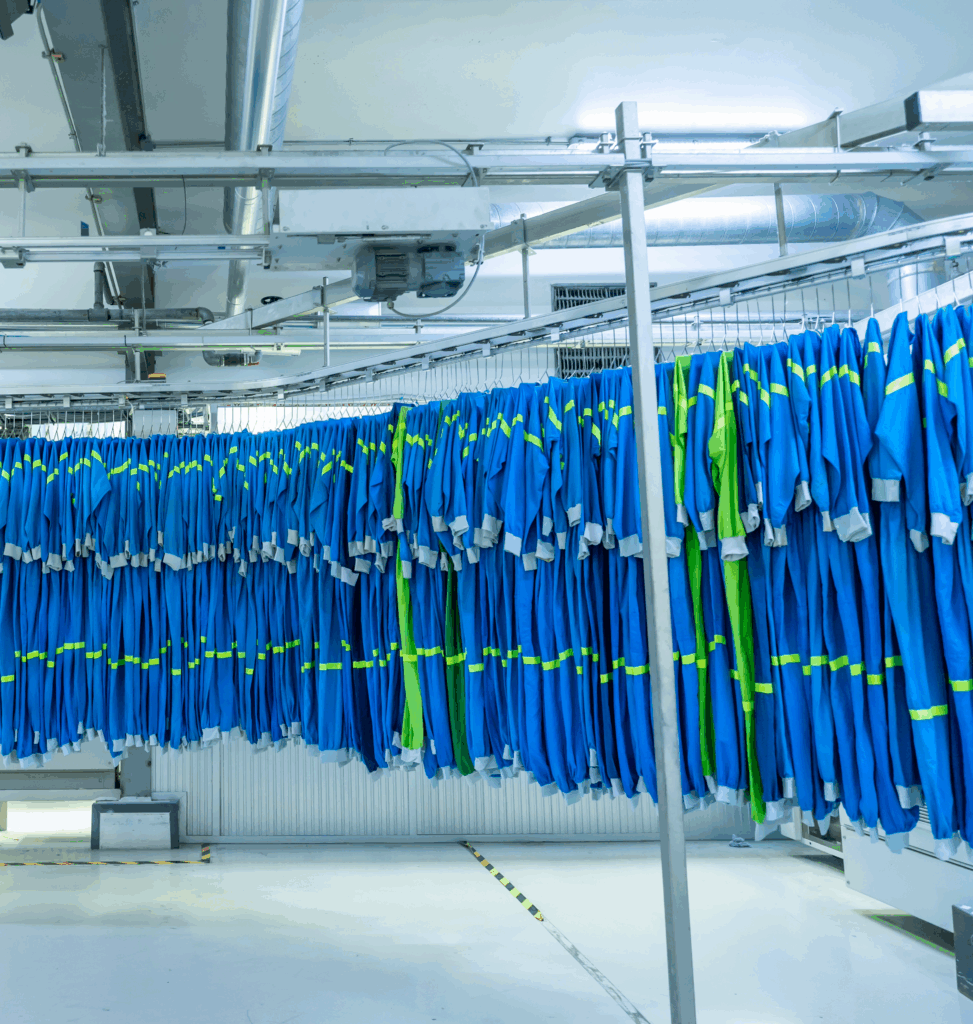 Tute da lavoro appese su un nastro trasportatore all'interno di una lavanderia industriale