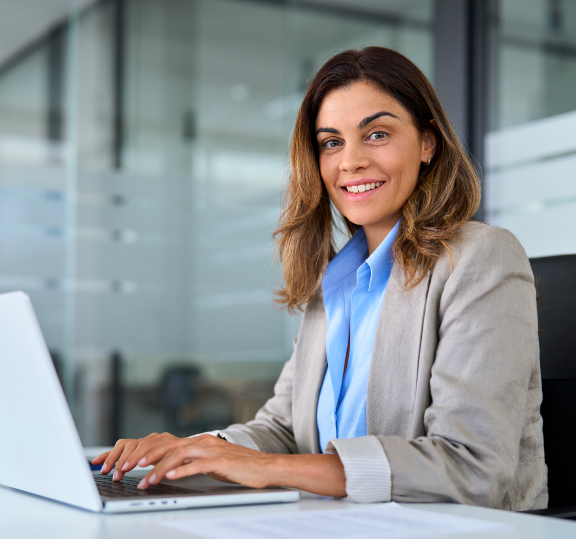 Una professionista sta lavorando sul computer portatile all'interno del proprio ufficio. Sta guardando verso l'obbiettivo sorridendo.