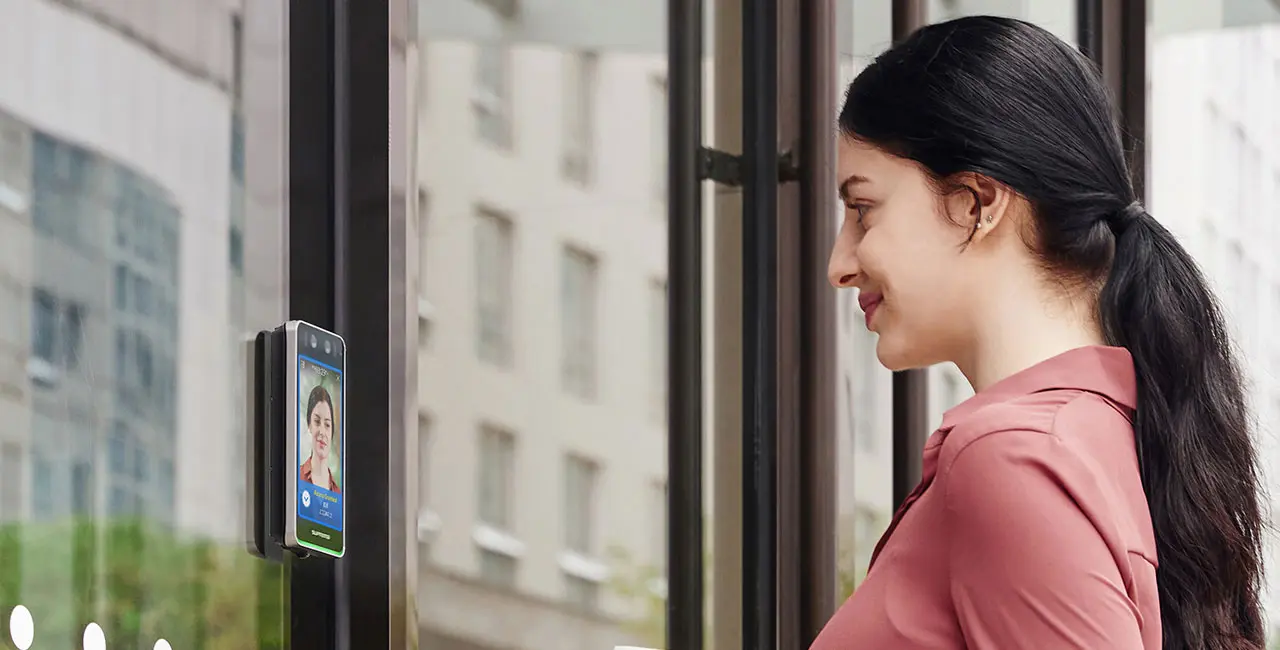 Ragazza sorridente di profilo davanti ad un dispositivo biometrico di riconoscimento facciale. 
