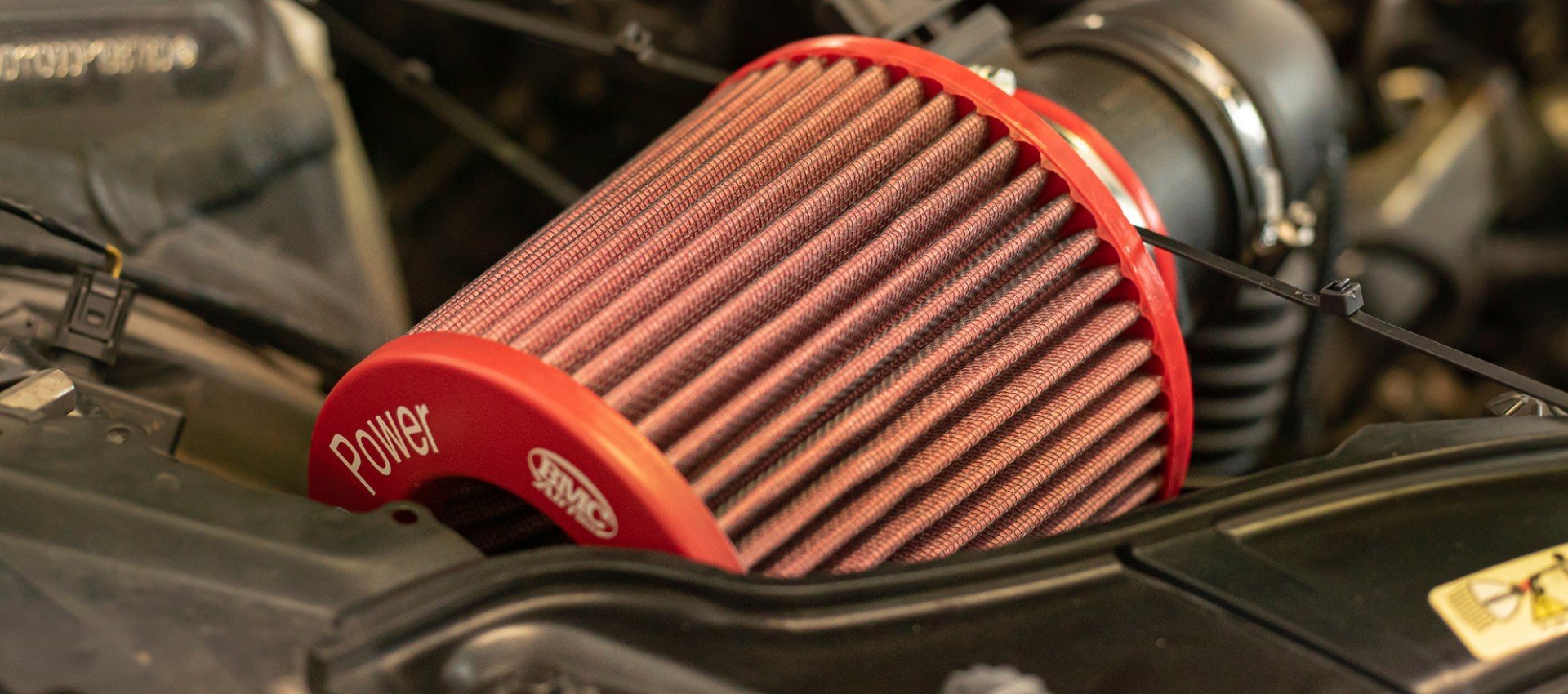 Dettaglio di un filtro dell'aria conico BMC Air Filter ad alte prestazioni installato nel vano motore di un'auto.