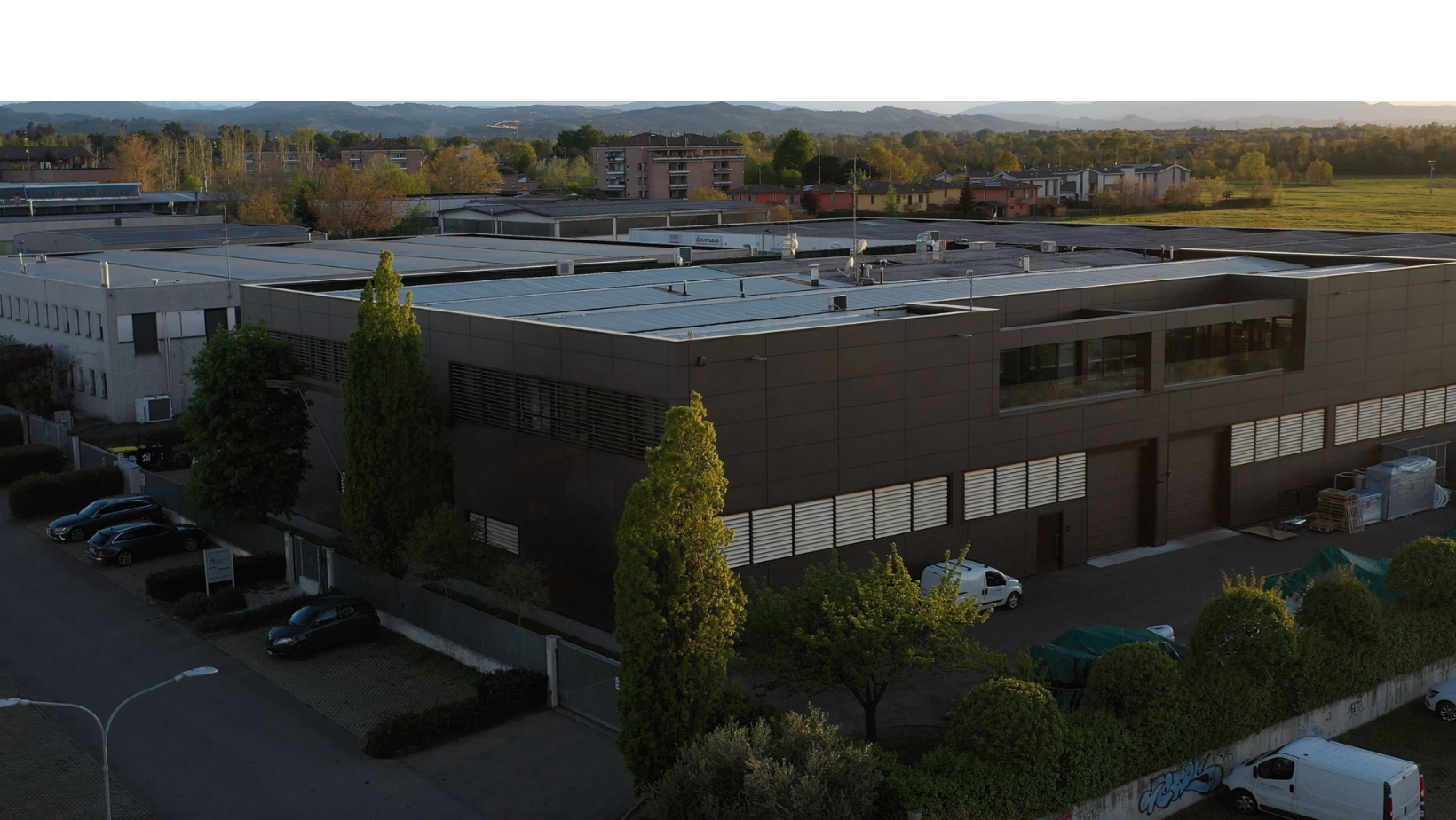 Veduta aerea della moderna sede di Torreggiani S.p.A., un ampio complesso industriale con facciata scura e pannelli fotovoltaici sul tetto, circondato dal verde.